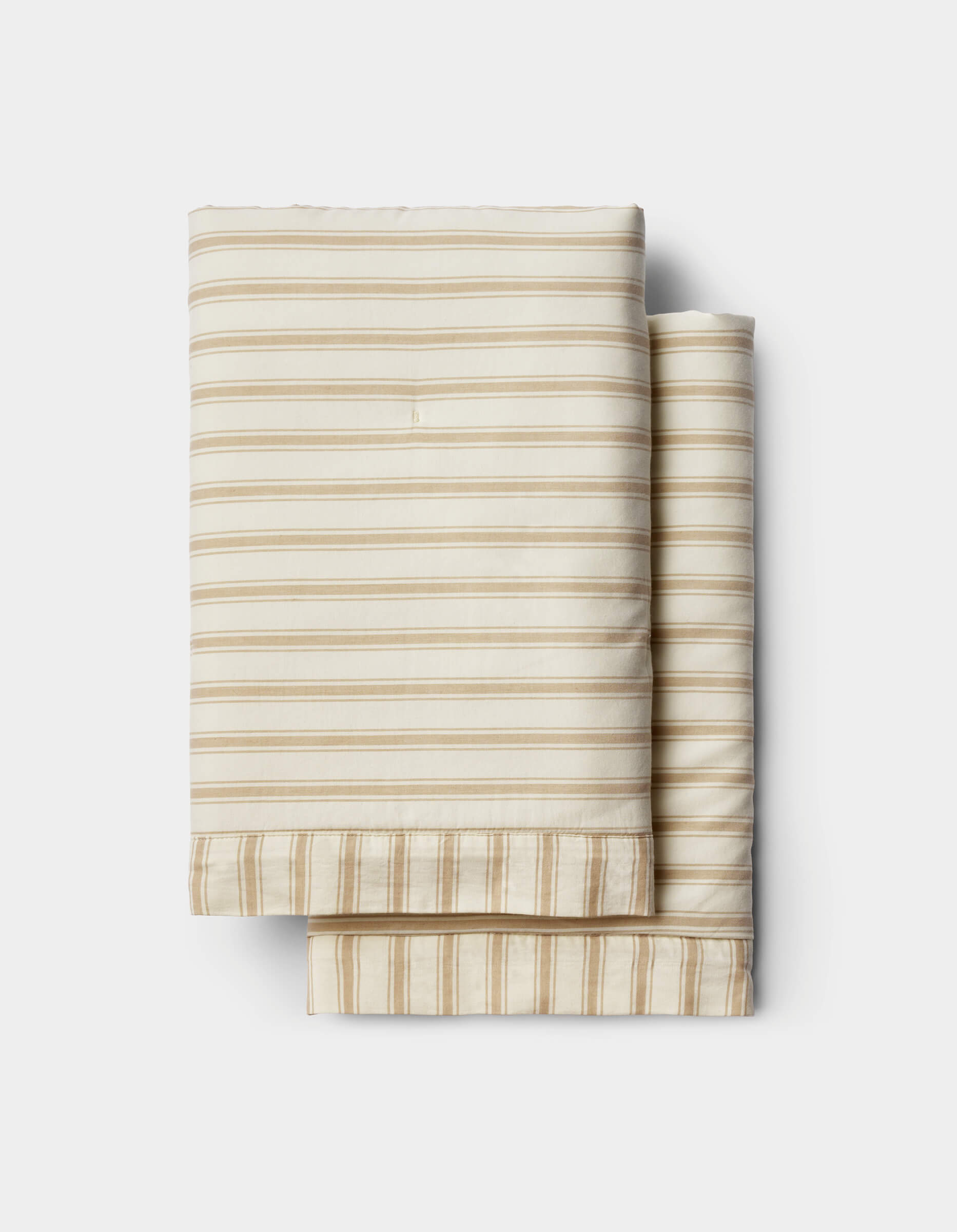 Cozy Earth’s Soft-Wash Cotton Duvet Set in beige and white stripes is neatly folded and stacked on a white background.