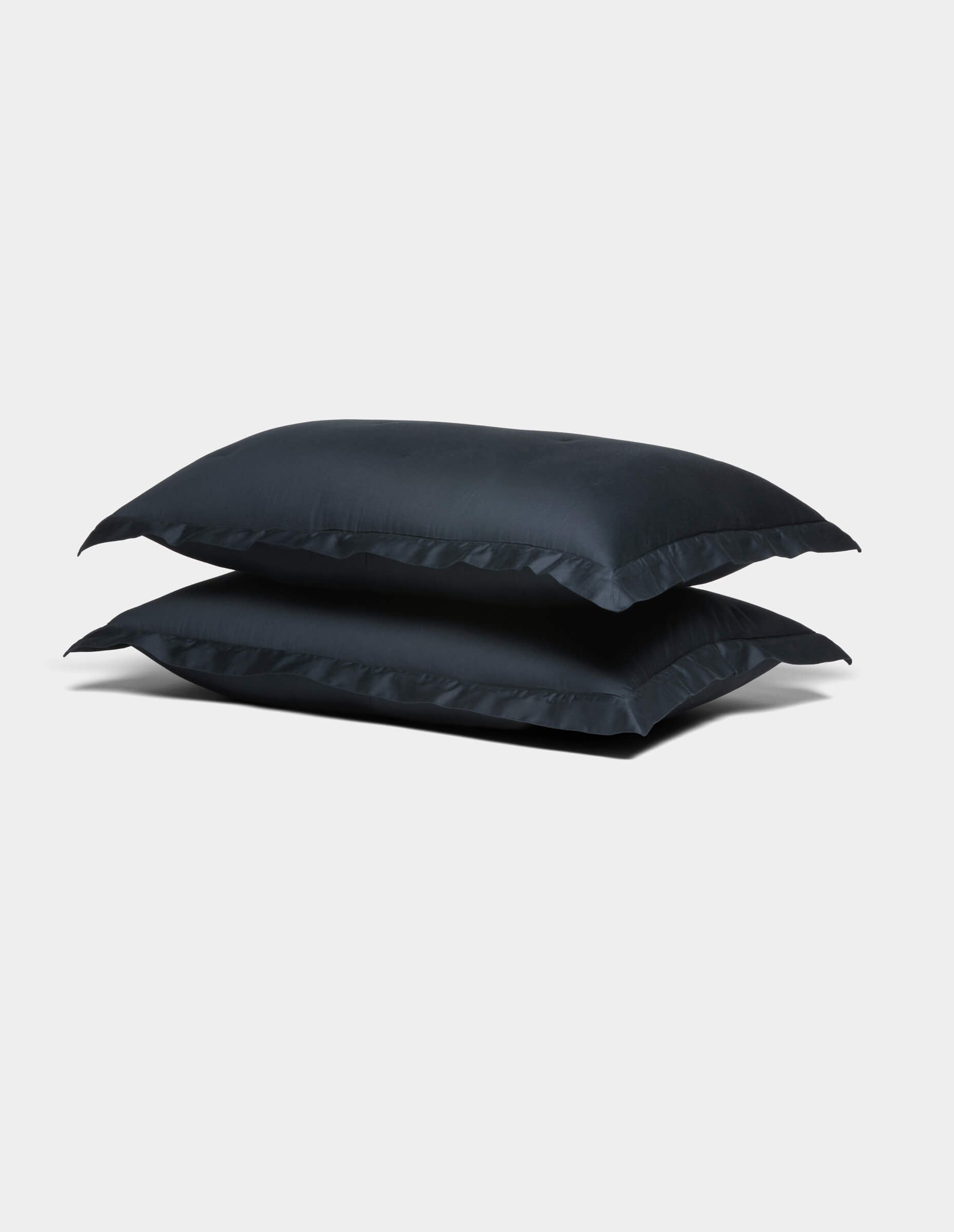 Two Cozy Earth Soft-Wash Cotton Shams in dark blue are stacked on top of each other against a plain light gray background.|Color:Eclipse