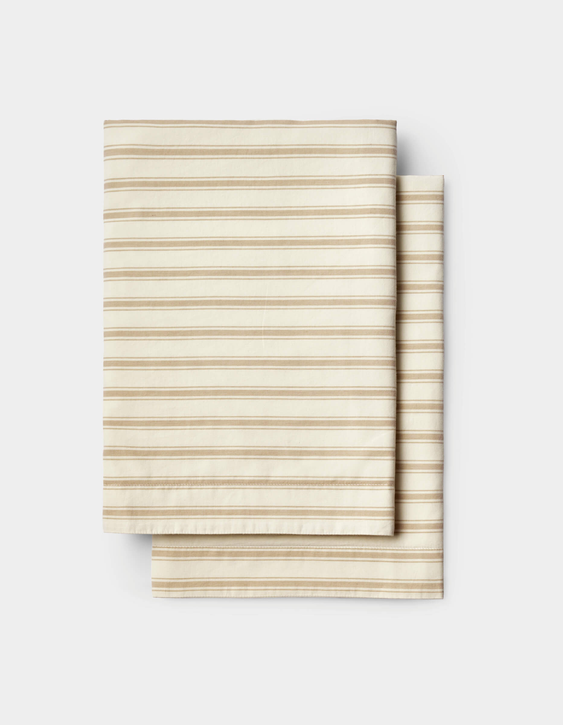 Neatly stacked on a white background, the Cozy Earth Soft-Wash Cotton Sheet Set features folded beige fabric with thin, evenly spaced horizontal brown stripes.
