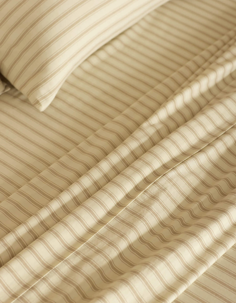 Close-up of a neatly made bed featuring the Cozy Earth Soft-Wash Cotton Sheet Set in beige and cream stripes. The smooth fabric and evenly spaced stripes create a calm, cozy atmosphere.