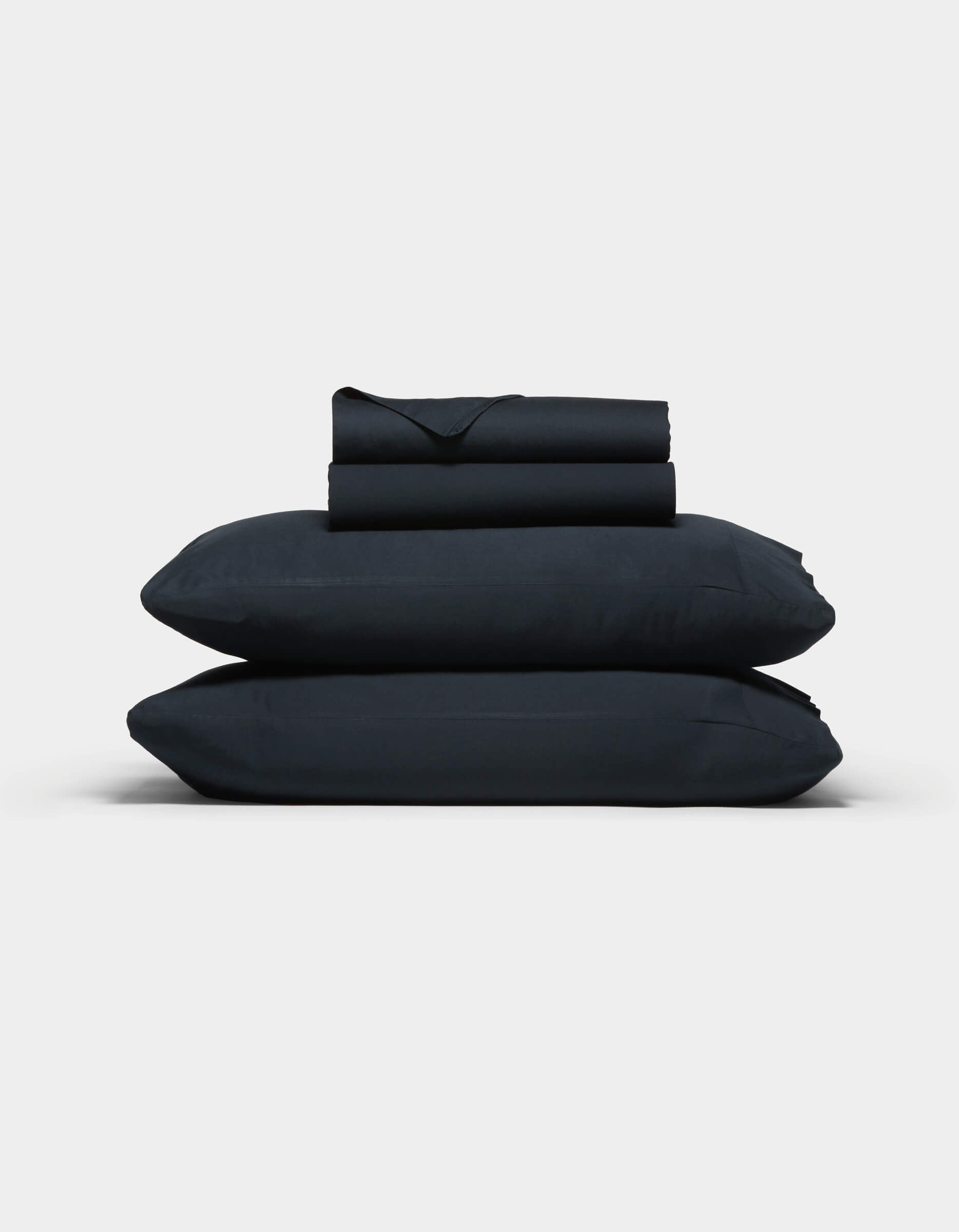 The Cozy Earth Soft-Wash Cotton Sheet Set, in dark navy blue, features two stacked pillows and folded sheets neatly arranged against a plain light gray background.|Color:Eclipse