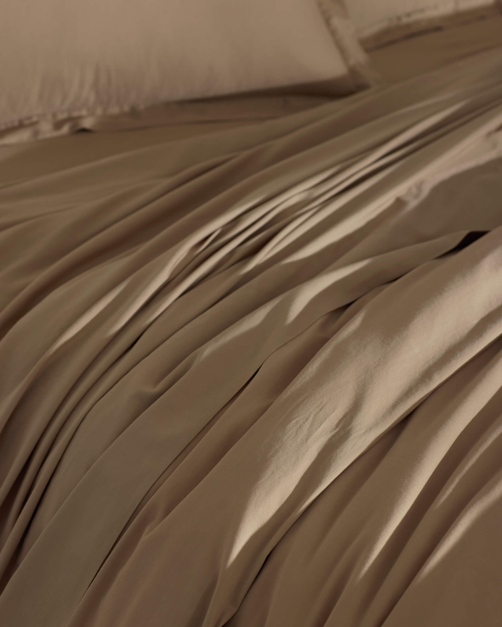 The Cozy Earth Soft-Wash Cotton Duvet Cover in brown is spread over the bed, creating gentle folds and shadows. Its smooth surface looks inviting, with matching pillowcases partially visible in the background.