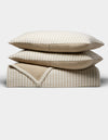 The Cozy Earth Waterfront Coverlet Bundle features two beige and white striped pillows stacked on a matching folded quilt, all set against a plain white background.|Color:Sandalwood Stripe