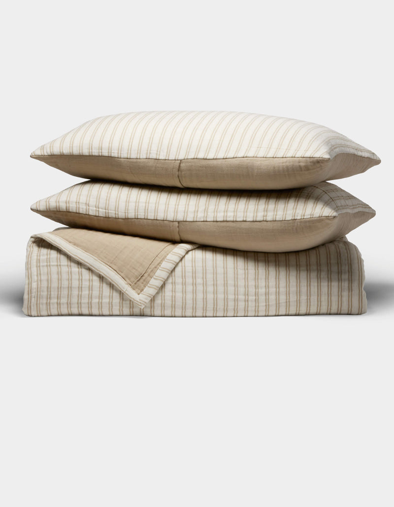 The Cozy Earth Waterfront Coverlet Bundle features two beige and white striped pillows stacked on a matching folded quilt, all set against a plain white background.