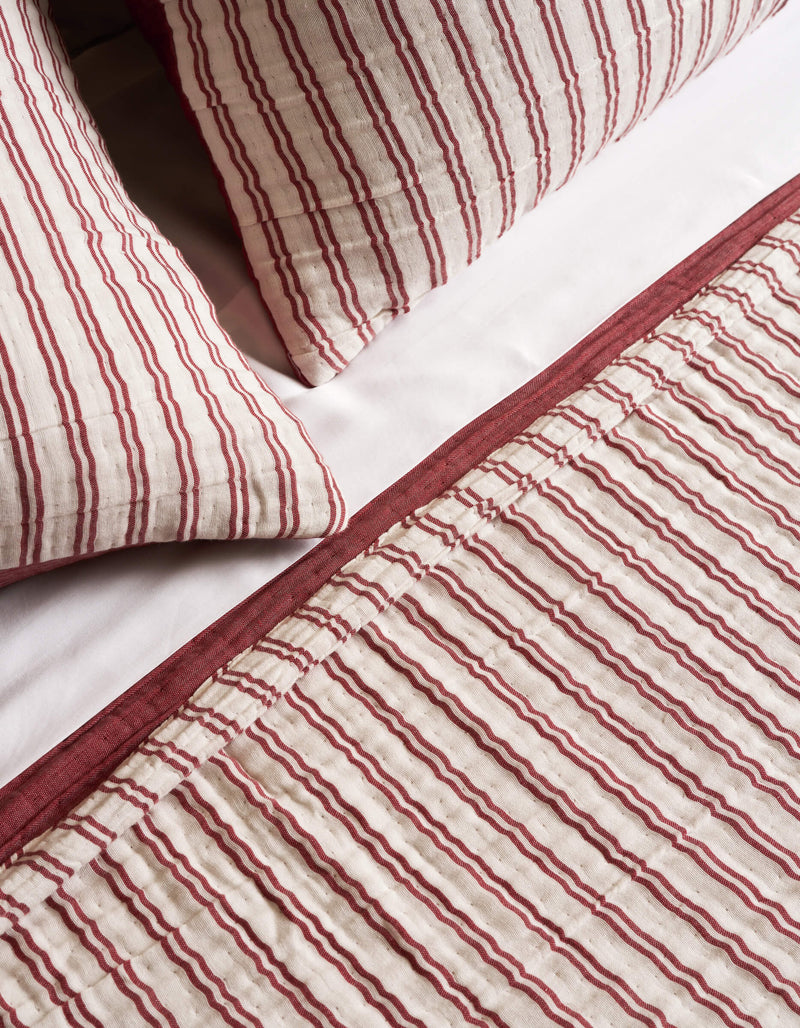 The Cozy Earth Waterfront Coverlet, featuring red and white vertical stripes with a solid red border, is shown on a bed with white sheets and two pillows.