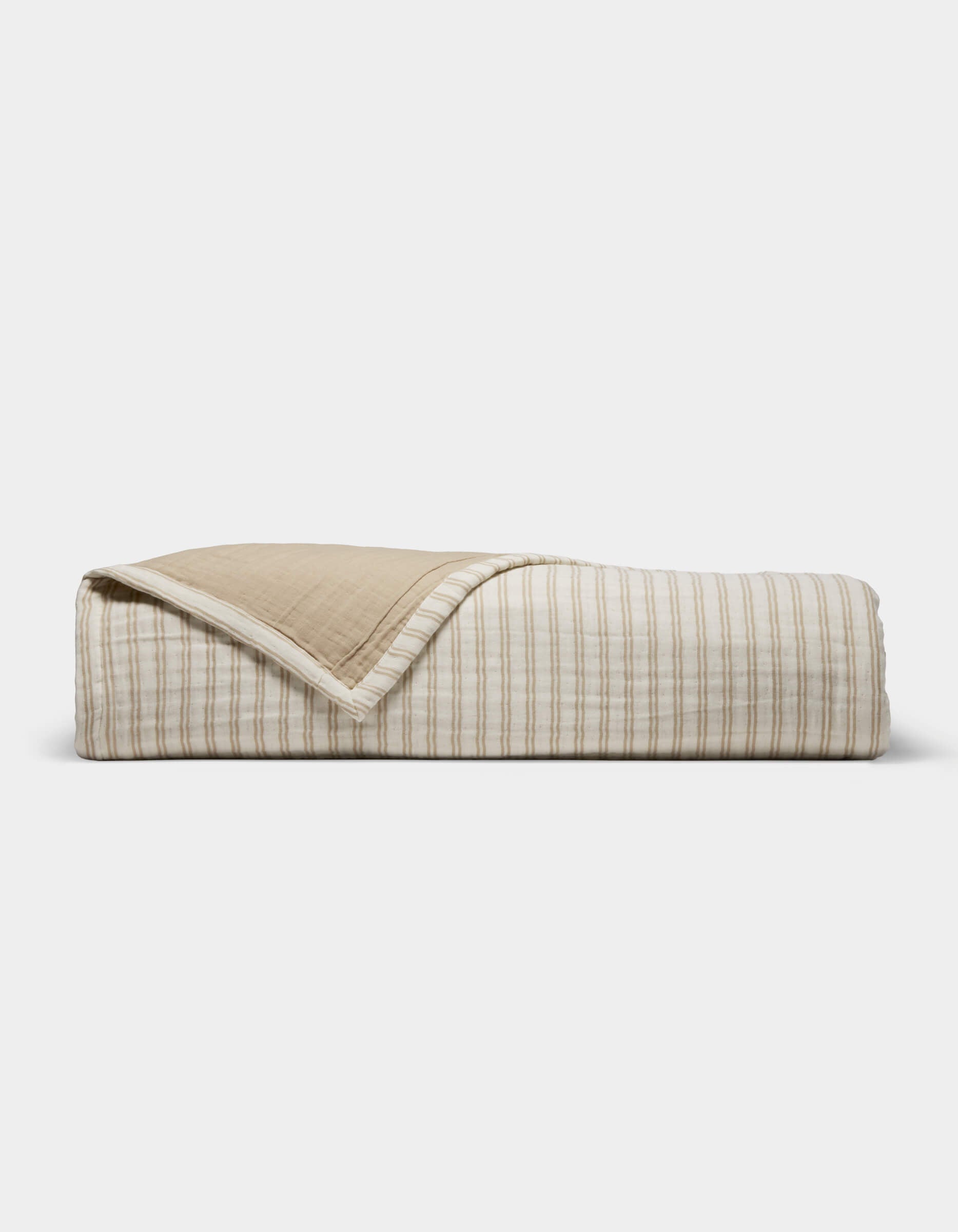The Cozy Earth Waterfront Coverlet, featuring beige and white stripes on one side and solid beige on the reverse, is shown neatly folded against a simple light backdrop.|Color:Sandalwood Stripe