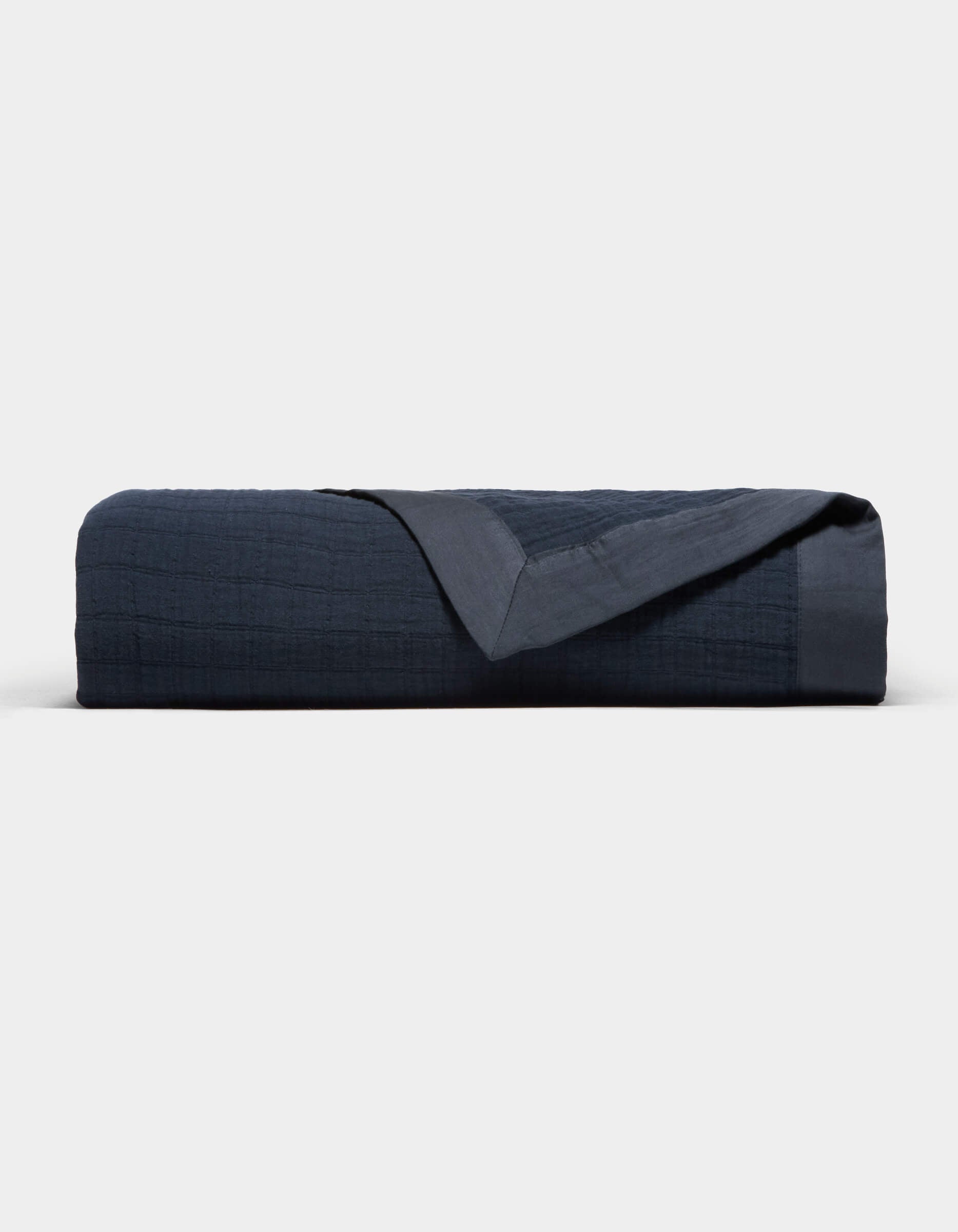 The Cozy Earth Waterfront Grid Matelasse Blanket is neatly folded in dark navy blue, showcasing its smooth, textured surface with one corner turned over, set against a plain light background.