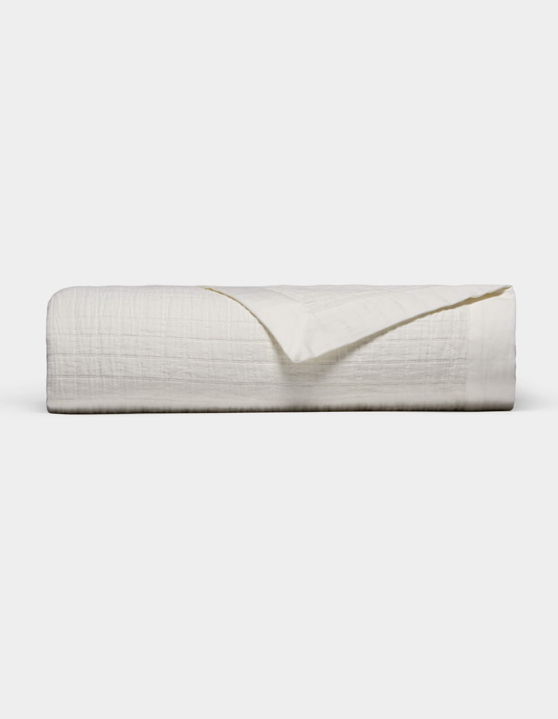 The Waterfront Grid Matelasse Blanket by Cozy Earth is shown neatly folded with a textured, crinkled surface against a plain light background. One corner is flipped over to reveal the underside.|Color:Sea Salt