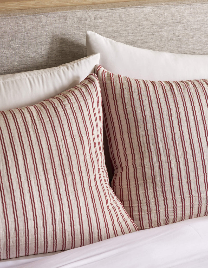 Two Cozy Earth Waterfront Shams with red and off-white vertical stripes rest against a light upholstered headboard, with a plain white pillow behind them and white bedding below.