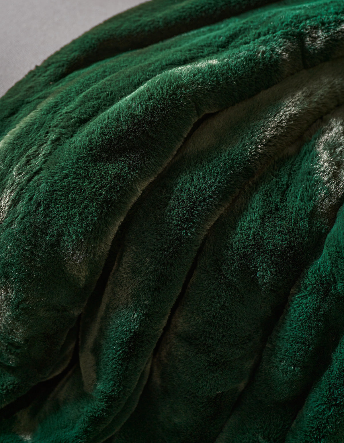 A close-up of the Cozy Earth Channel Cuddle Blanket in plush, dark green faux fur, draped in soft, wavy folds to highlight its velvety texture and elegant sheen.