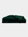 A Cozy Earth Channel Cuddle Blanket in dark green, featuring plush fur, is neatly folded and stacked against a plain white background.|Color:Emerald
