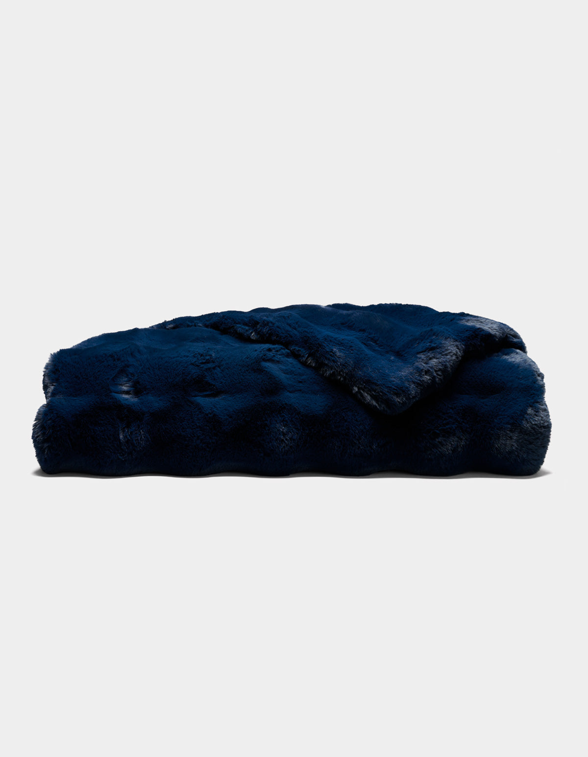 A folded Double Bubble Cuddle Blanket by Cozy Earth, in plush dark blue faux fur, rests on a plain light background. The blanket appears thick, soft, and cozy, featuring a slightly shiny texture.|Color:Eclipse
