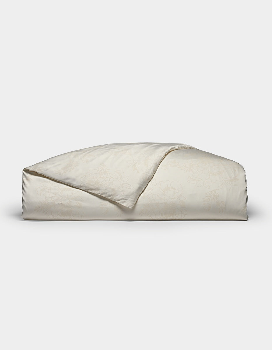 A folded Bamboo Duvet Cover by Cozy Earth in a light cream color with a subtle floral pattern is displayed on a plain white background.|Color:Sonoma Floral in Vintage White