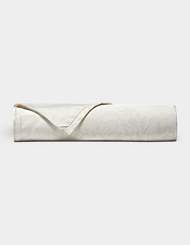 A neatly rolled Cozy Earth Bamboo Flat Sheet in cream, featuring a subtle floral pattern and a folded-back hemmed corner, displayed on a plain white background.