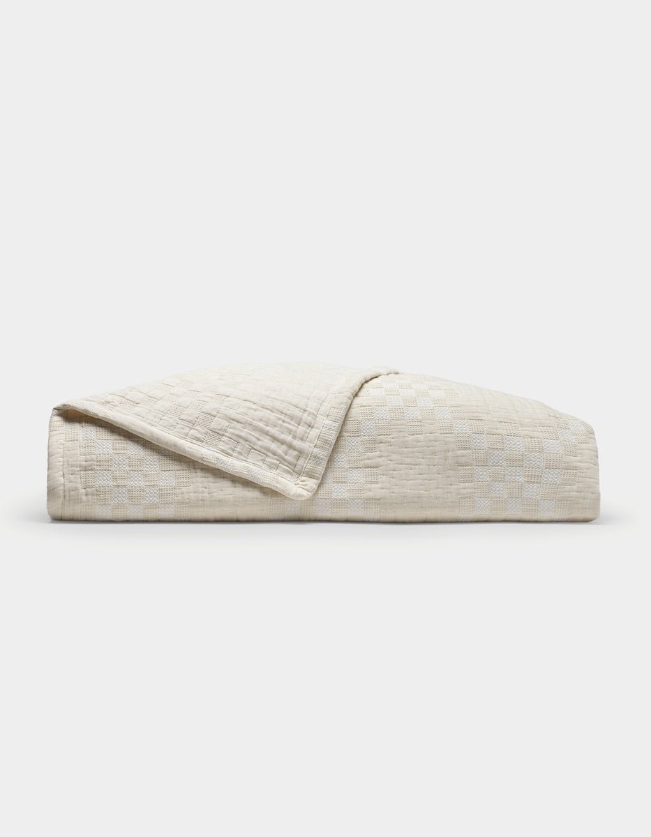 A neatly folded Sonoma Stitch Quilt by Cozy Earth in Vintage White, featuring a subtle checkered pattern, displayed against a plain white background.
