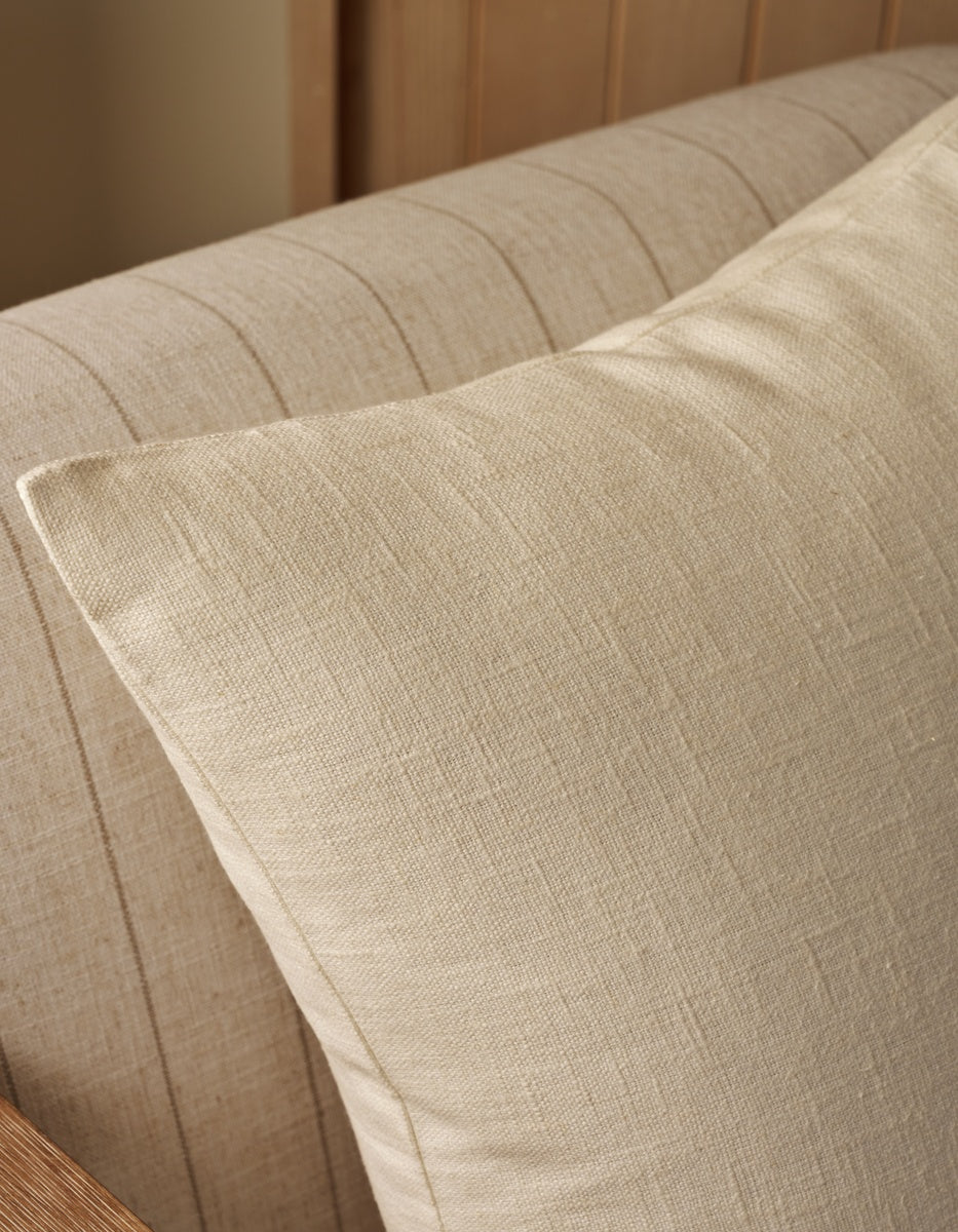 A close-up of the Cozy Earth Sonoma Throw Pillow in beige, featuring a textured design and resting against the matching backrest of a fabric upholstered sofa or chair with wood accents.