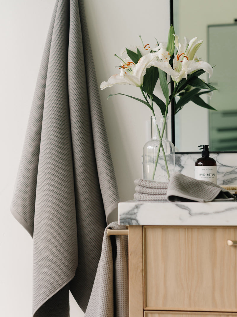 Waffle Bath Towel in the color Charcoal. Photo of Charcoal Waffle Bath Towel taken with Charcoal Waffle Bath Towel hanging from towel hook in a bathroom with white walls