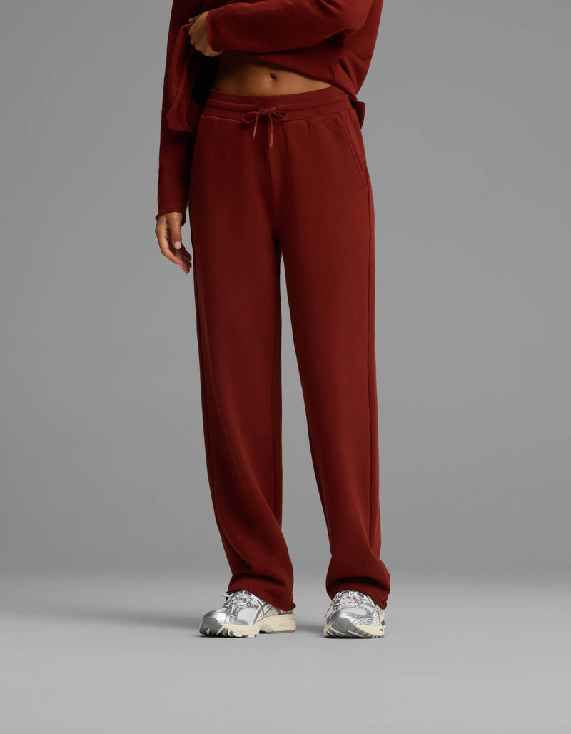 A person wearing the Women's Chelsea Set by Cozy Earth in maroon, paired with silver sneakers, stands against a plain gray background. The person's face is not visible.