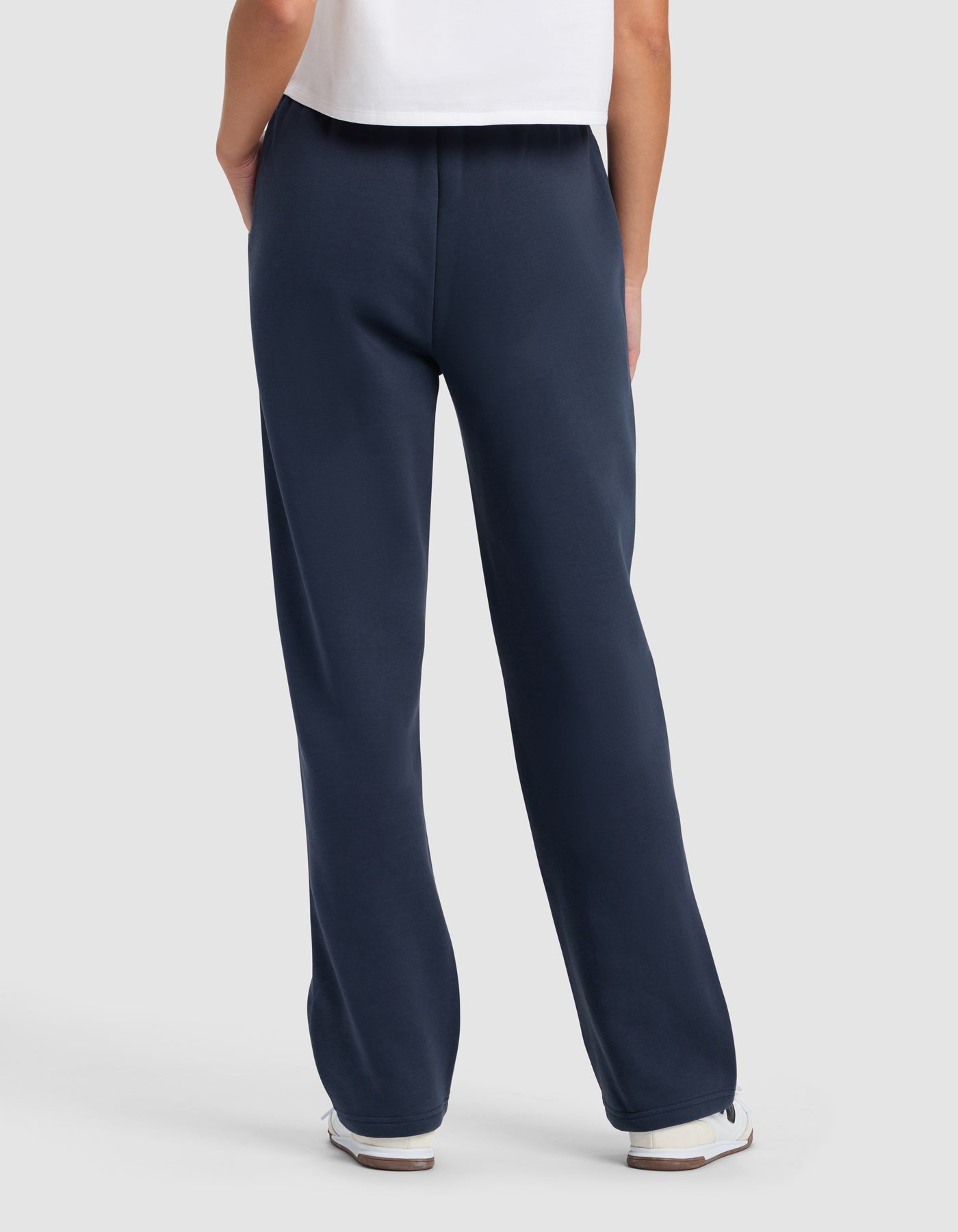 A person faces away, wearing Cozy Earth's Women's Cityscape 2.0 Wide Leg Pant in navy, paired with a white t-shirt and white sneakers, set against a plain light background.|Color:Eclipse