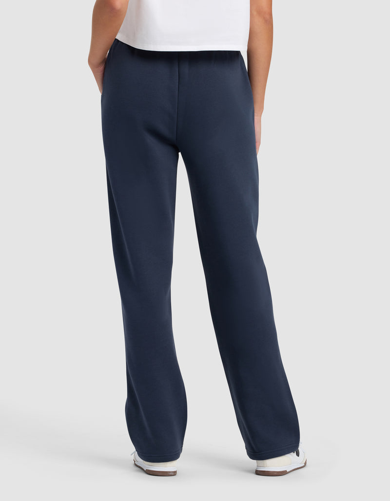 A person faces away, wearing Cozy Earth's Women's Cityscape 2.0 Wide Leg Pant in navy, paired with a white t-shirt and white sneakers, set against a plain light background.
