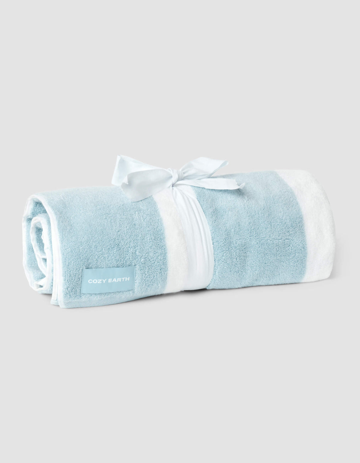 A Classic Stripe Resort Towel by Cozy Earth, rolled up in blue and white stripes, tied with a white ribbon and a "COZY EARTH" tag, displayed on a plain light gray background.
