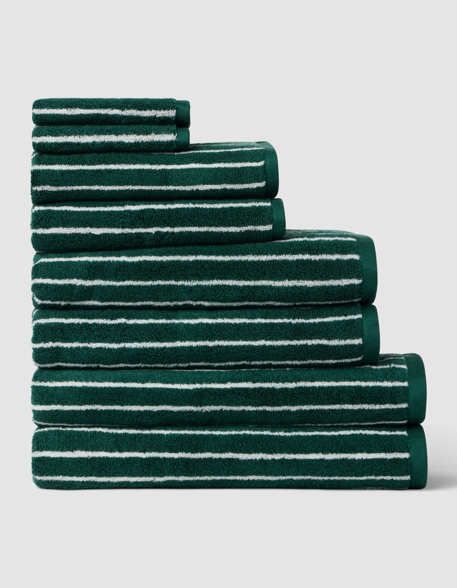 Six towels from the Complete Luxe Bath Bundle by Cozy Earth, featuring a uniform color with seashell stripe, stacked in descending size order on a light gray background.