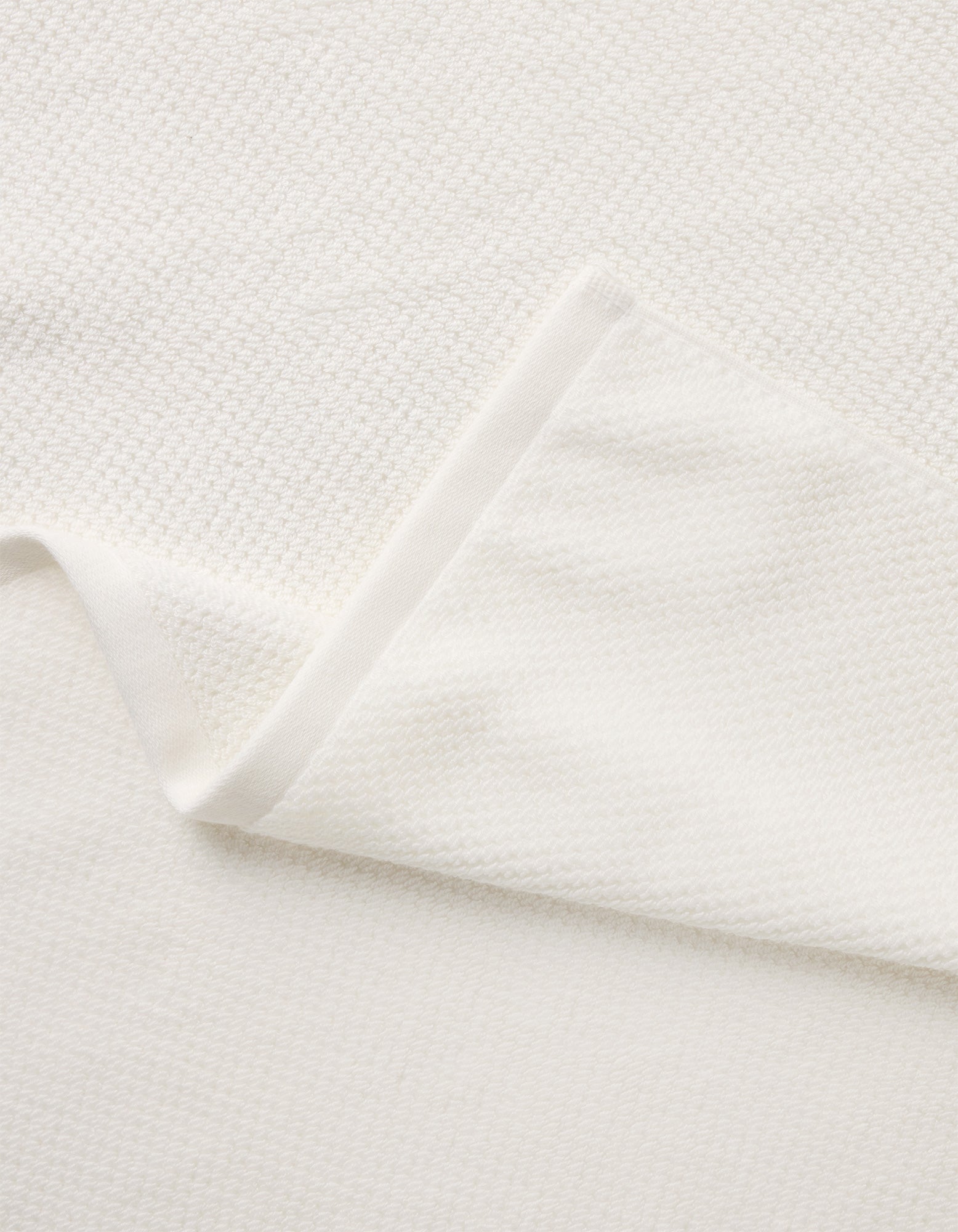 A close-up of the Nantucket Bath Towel Set by Cozy Earth shows its soft, white textured fabric, with a folded corner revealing the towel’s thickness and elegant woven pattern.|Color:White