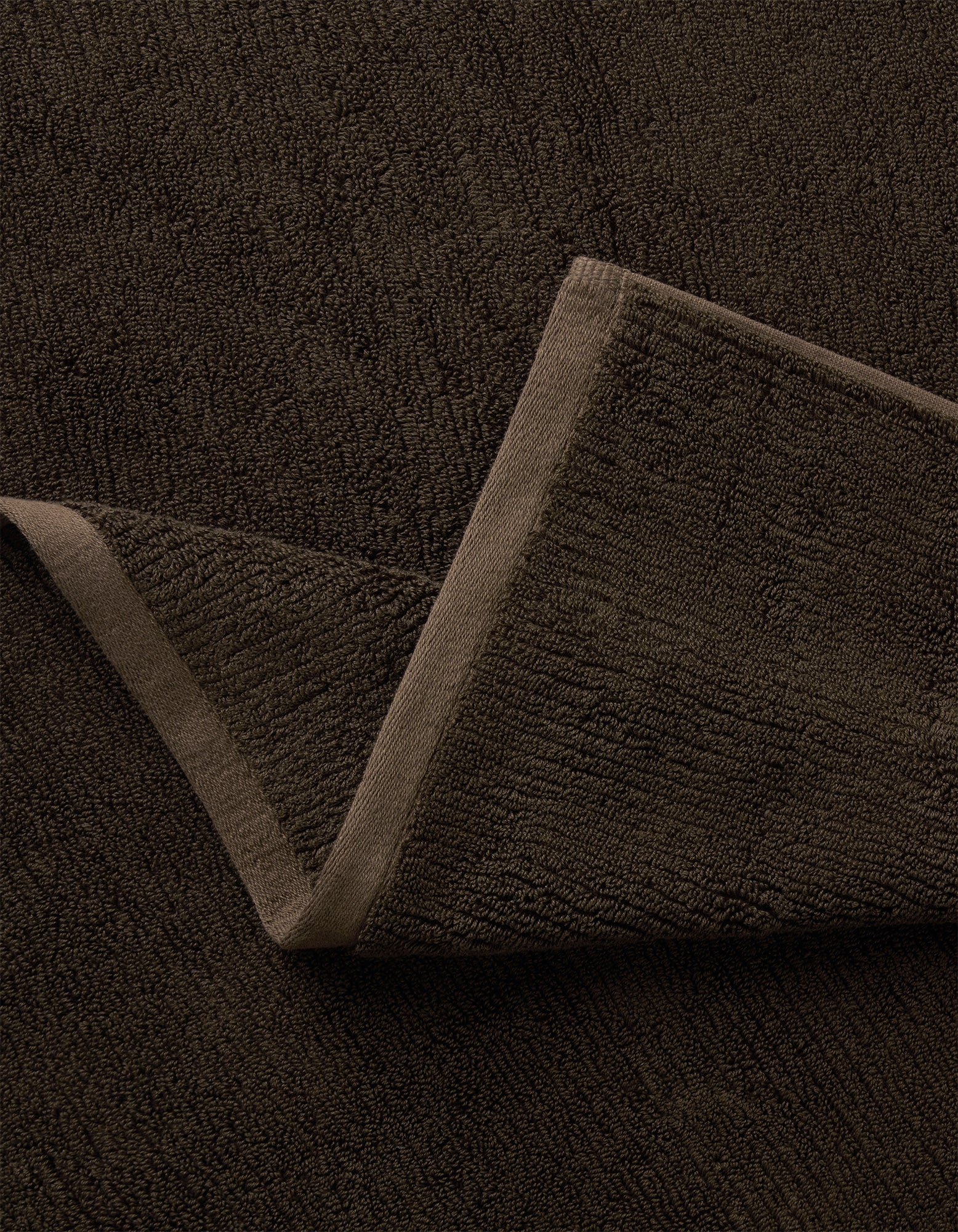 A close-up of the Complete Ribbed Terry Bath Bundle by Cozy Earth in dark brown, featuring one corner folded to reveal its soft ribbed fabric and stitched edges.|Color:Espresso