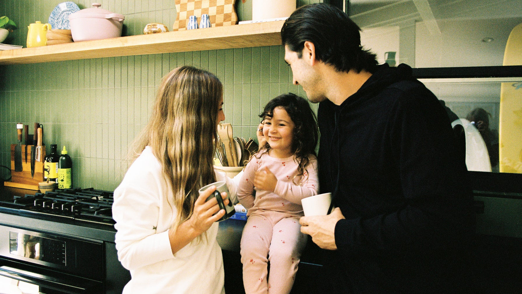 Family of three in a kitchen, with a child sitting on a counter.