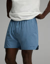 A person wearing a white shirt and Cozy Earth Men’s Day & Night Short 5″ in Nordic Blue, which features the brand’s name on the left leg, standing with hands on hips against a plain background.|Color:Nordic Blue