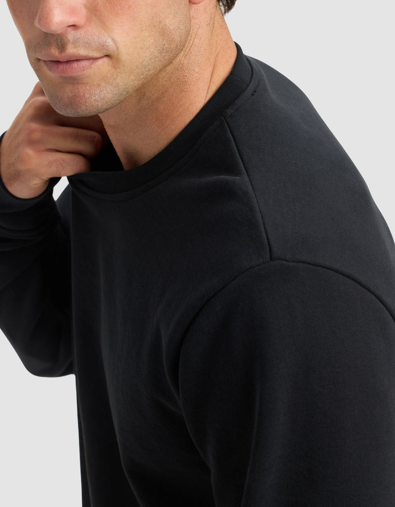 A man wearing the Cozy Earth Men's Dylan Crewneck is shown from the shoulders up, slightly turned to the side, with his hand touching the back of his neck against a light gray background.