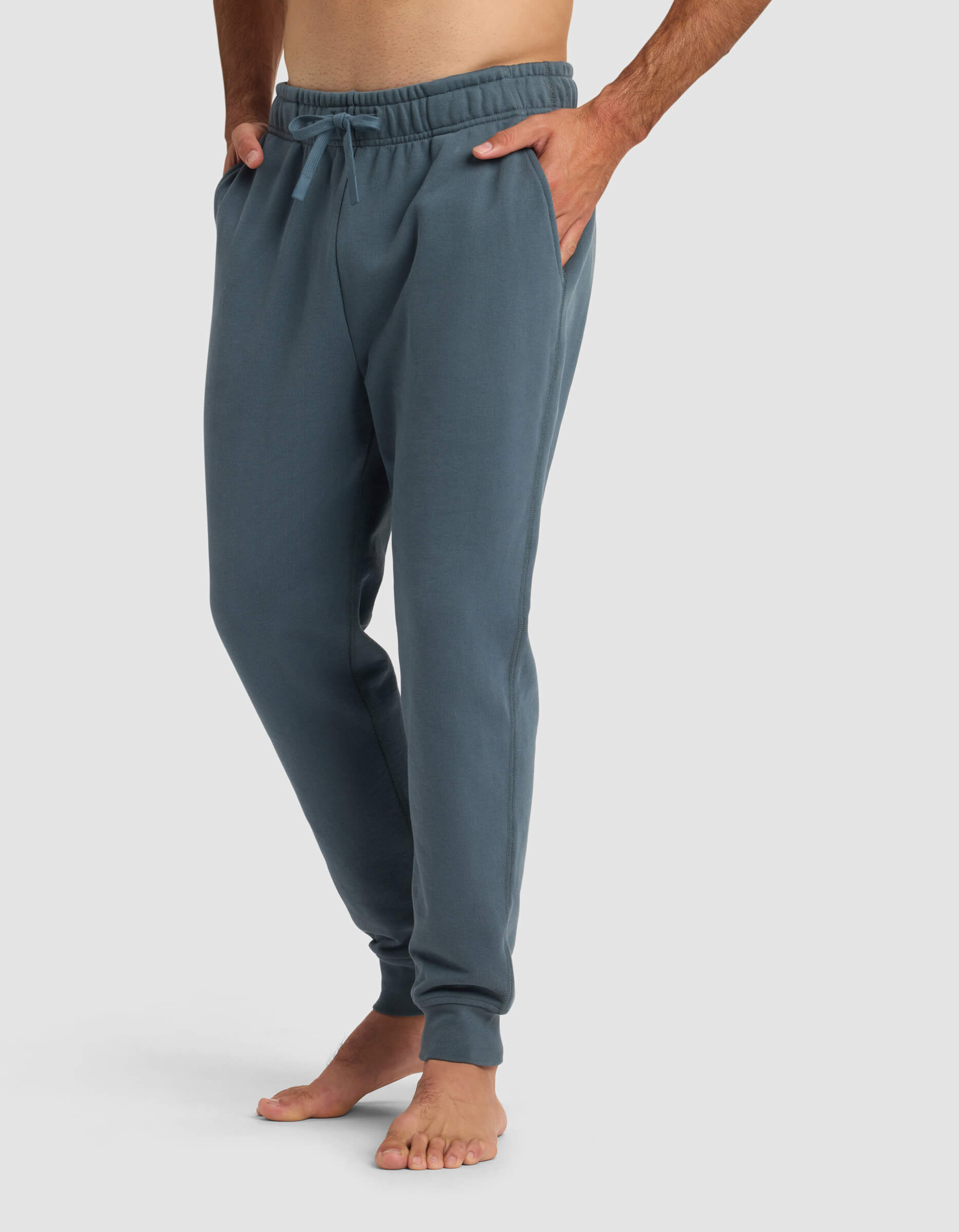 A person stands barefoot with hands in pockets, wearing Cozy Earth's Men's Dylan Jogger, against a plain light background.