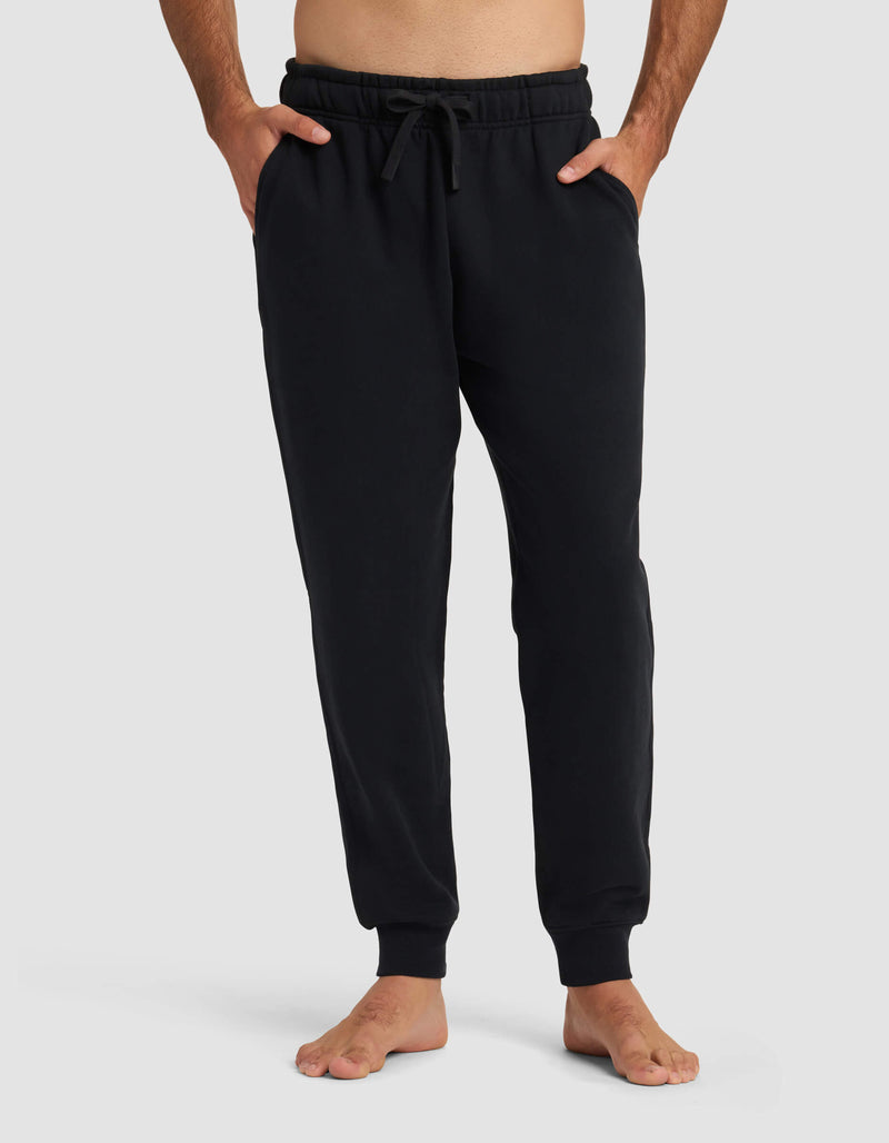 A person stands barefoot in Cozy Earth Men's Dylan Jogger in Jet Black, featuring an elastic waistband, drawstring, and side pockets. The background is plain light gray.