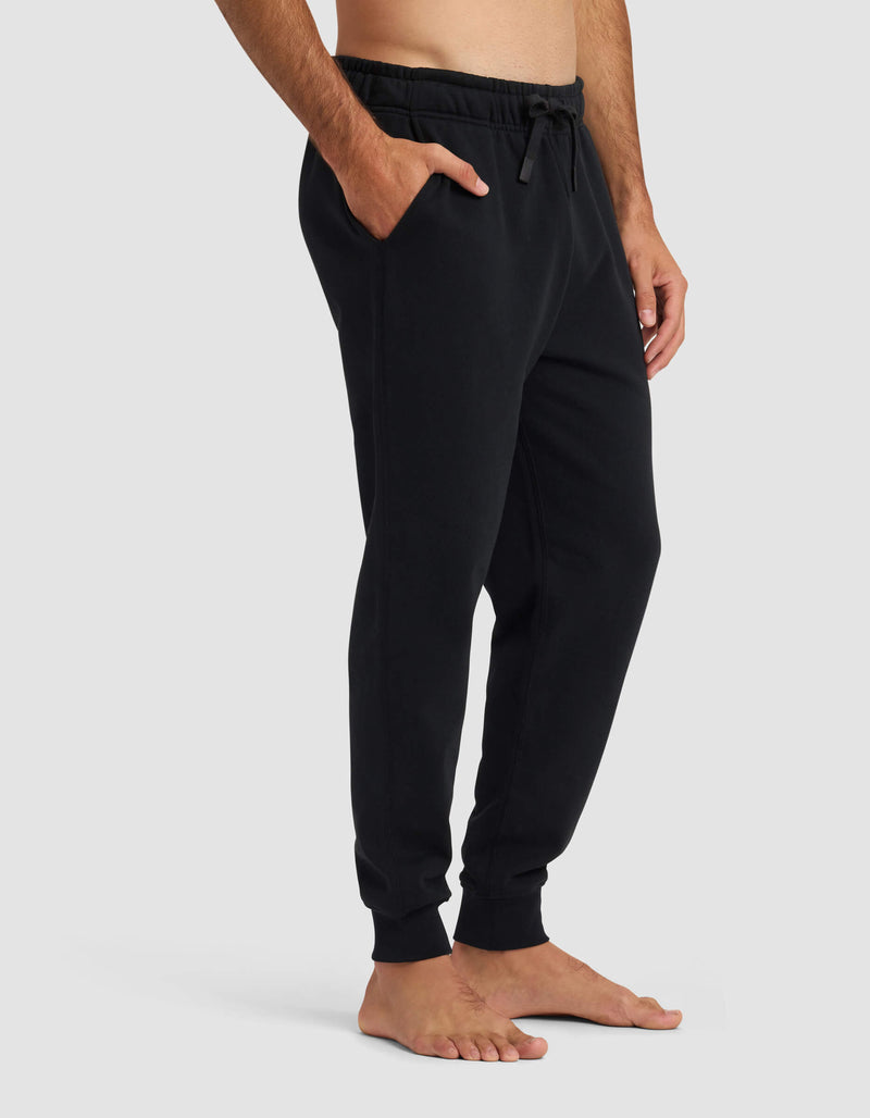 A man stands barefoot wearing Cozy Earth's Men's Dylan Jogger, featuring pockets and a drawstring waist, shown from mid-chest to feet against a plain light gray background.