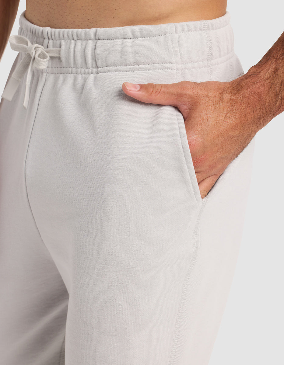 A person wearing Cozy Earth Men’s Dylan Jogger sweatpants in light gray has one hand in the pocket. The elastic waistband features a drawstring. The photo displays the pants from the waist to mid-thigh.