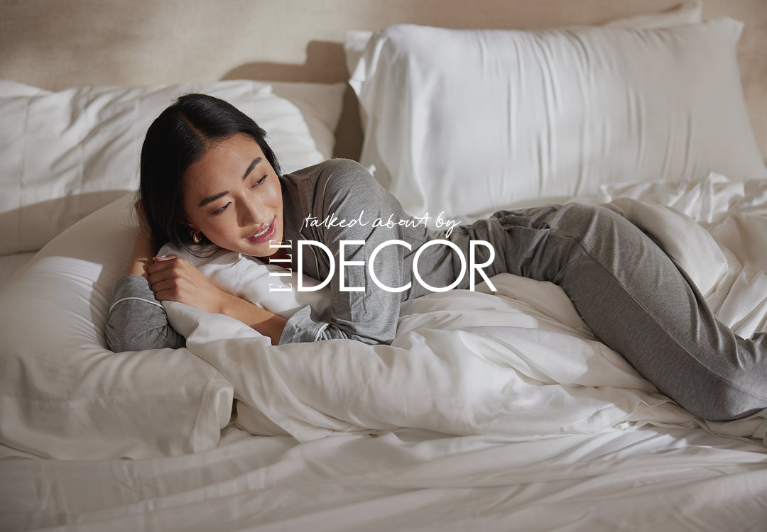 Woman lying on a bed with white bedding, wearing gray pajamas, with 'ELLE DECOR' logo overlay.