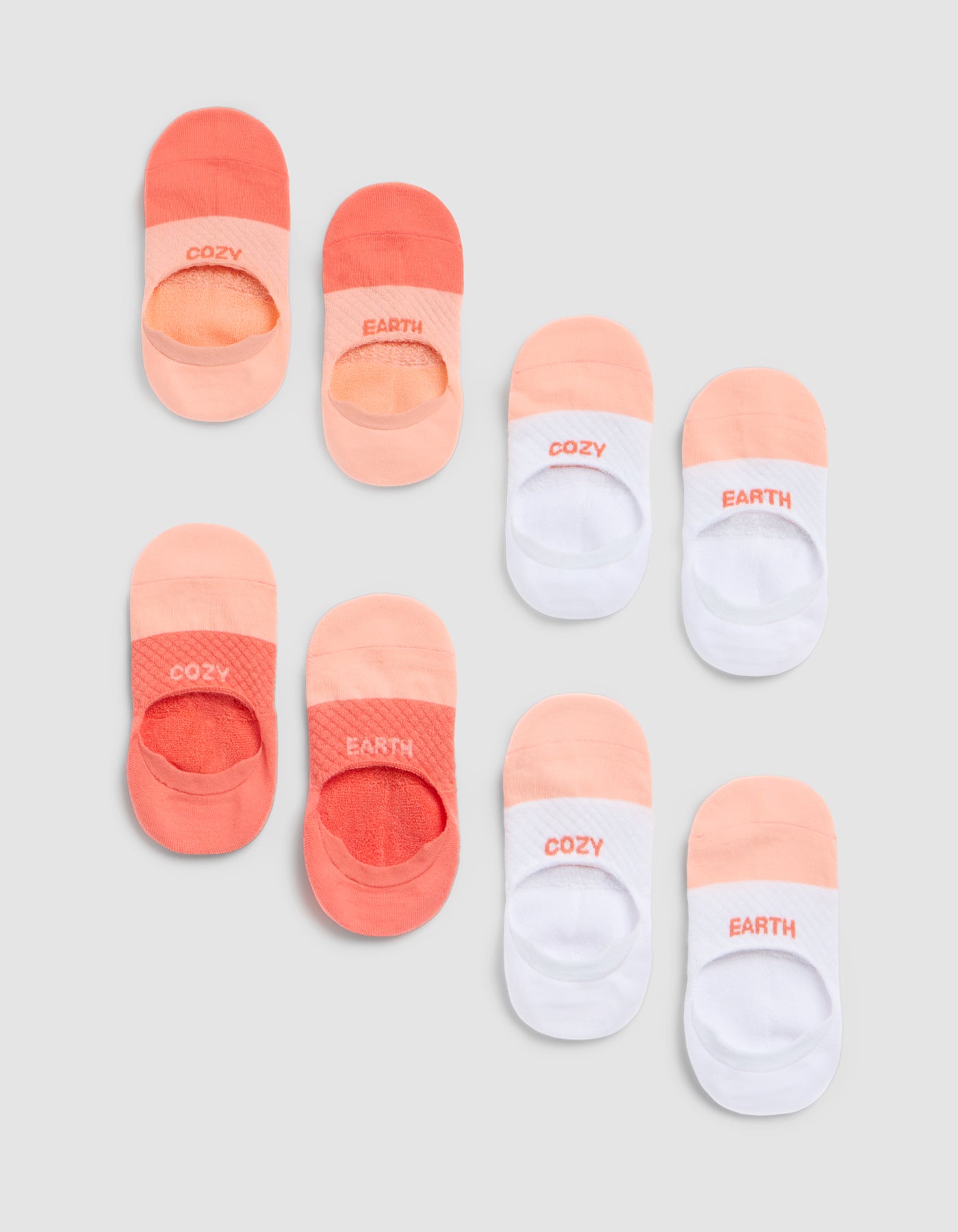 The Cozy Earth Essential No-Show Sock 4-Pack includes socks in peach, orange, and white tones with "COZY" or "EARTH" printed on the toes, shown arranged neatly on a light grey background. 