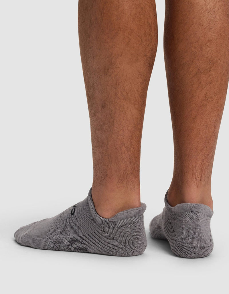 Back view of a person wearing Cozy Earth Essential Ankle Socks, low-cut gray socks that barely cover the ankles, standing on a white surface with lower legs visible.