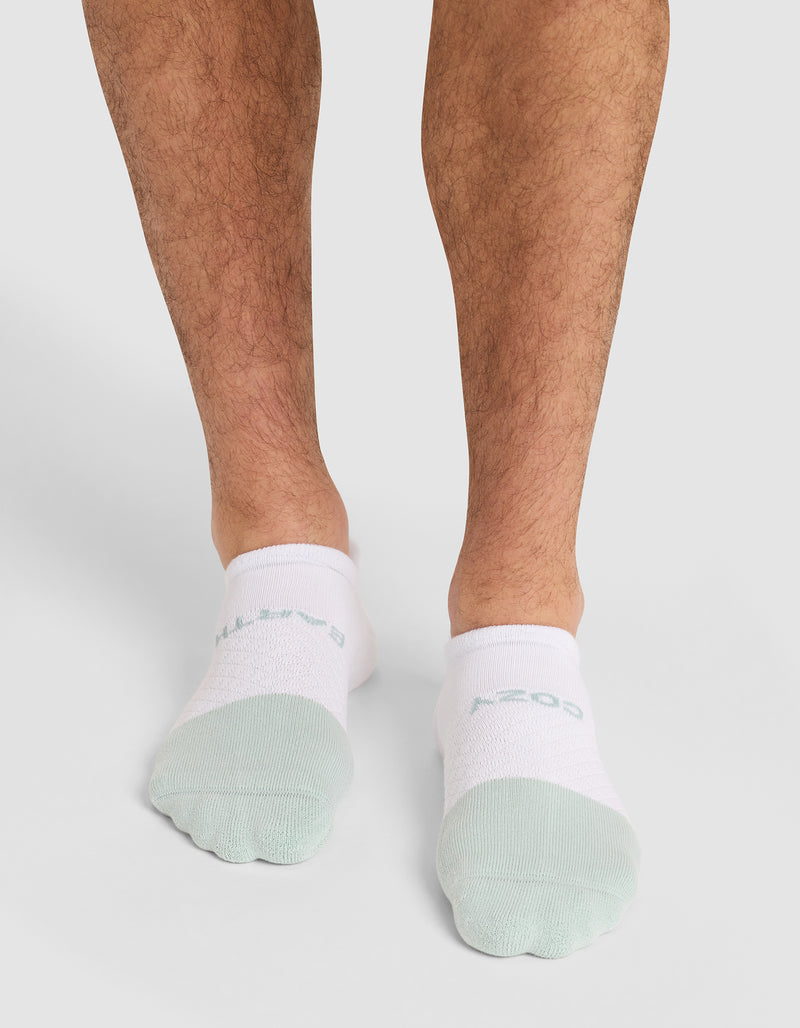 A person wears Cozy Earth Essential Ankle Socks in white and light green, standing on a light background with only their lower legs and feet visible.