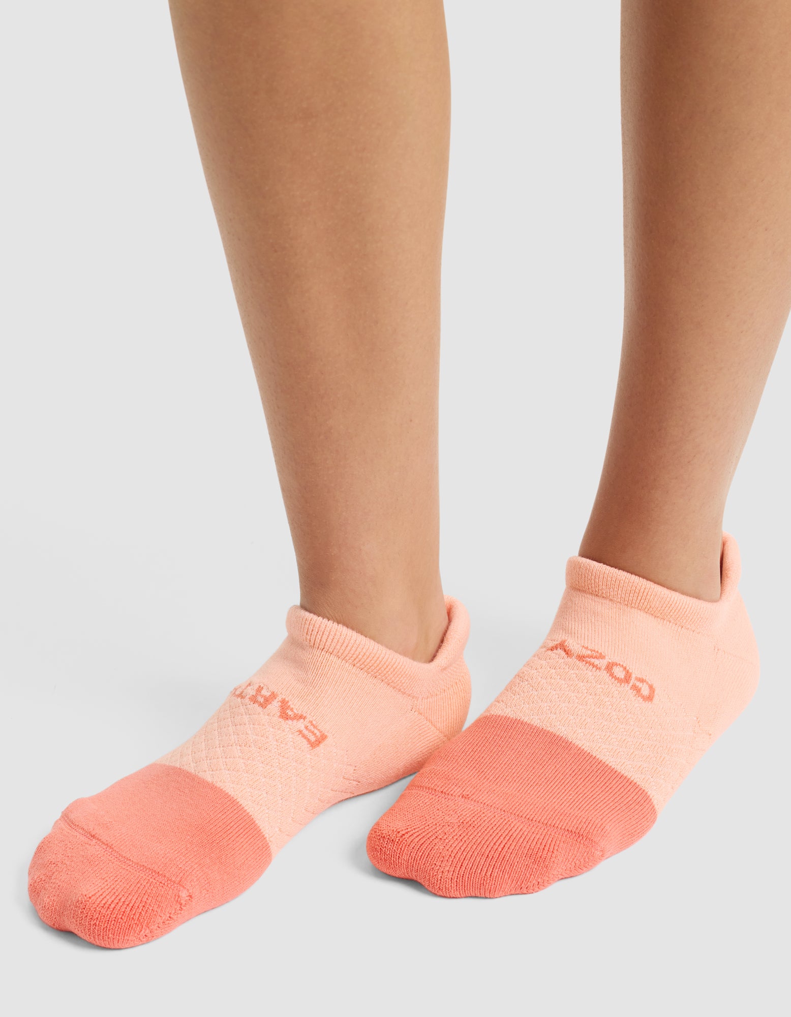 A person is wearing Cozy Earth's Essential Ankle Sock in light pink with a darker pink toe, standing on a light surface. Only their lower legs and feet are visible. |Color:Cantaloupe