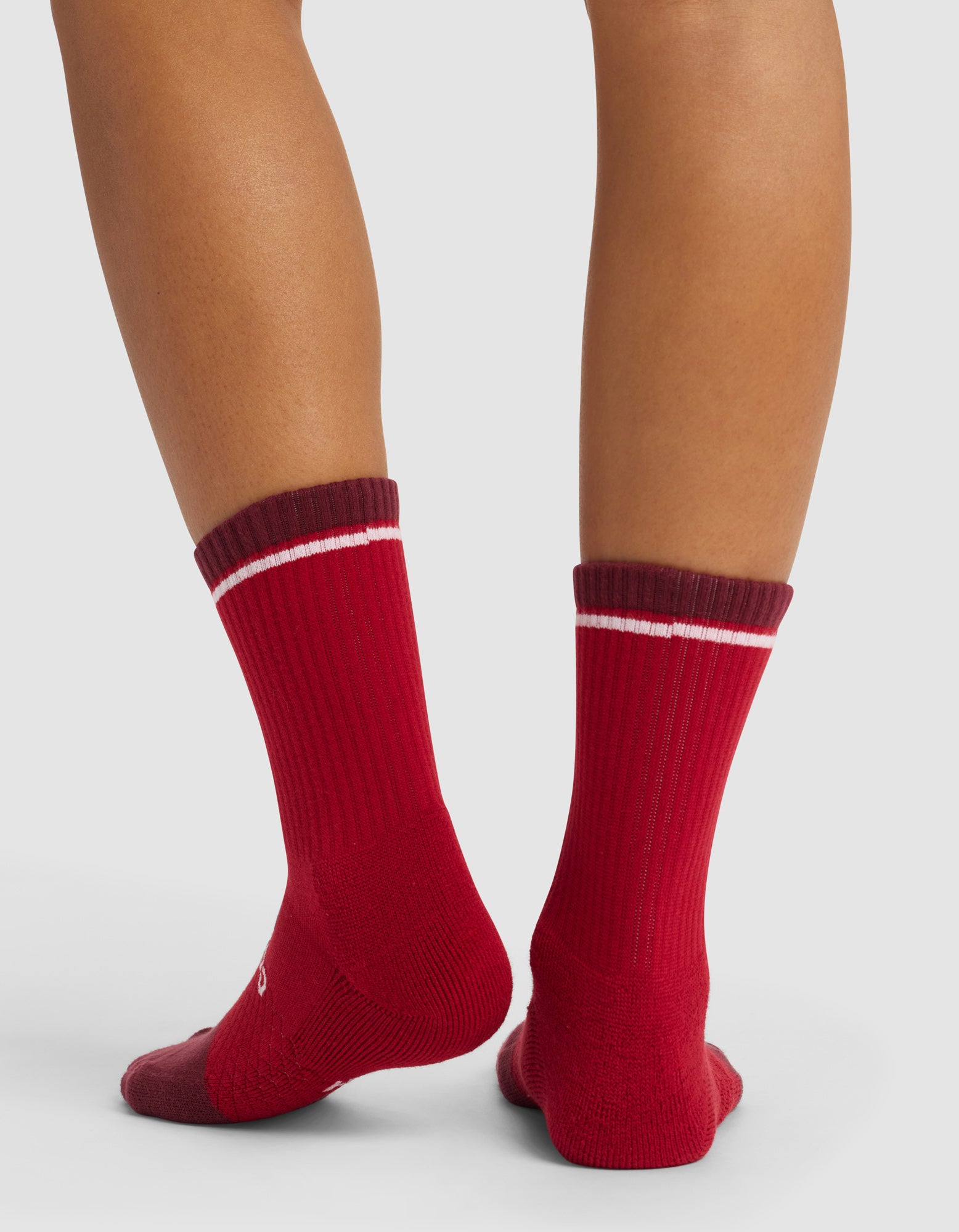 A person stands with their back to the camera, wearing Cozy Earth Essential Calf Socks—red with dark maroon cuffs and a white stripe—on a light background.|Color:Crimson