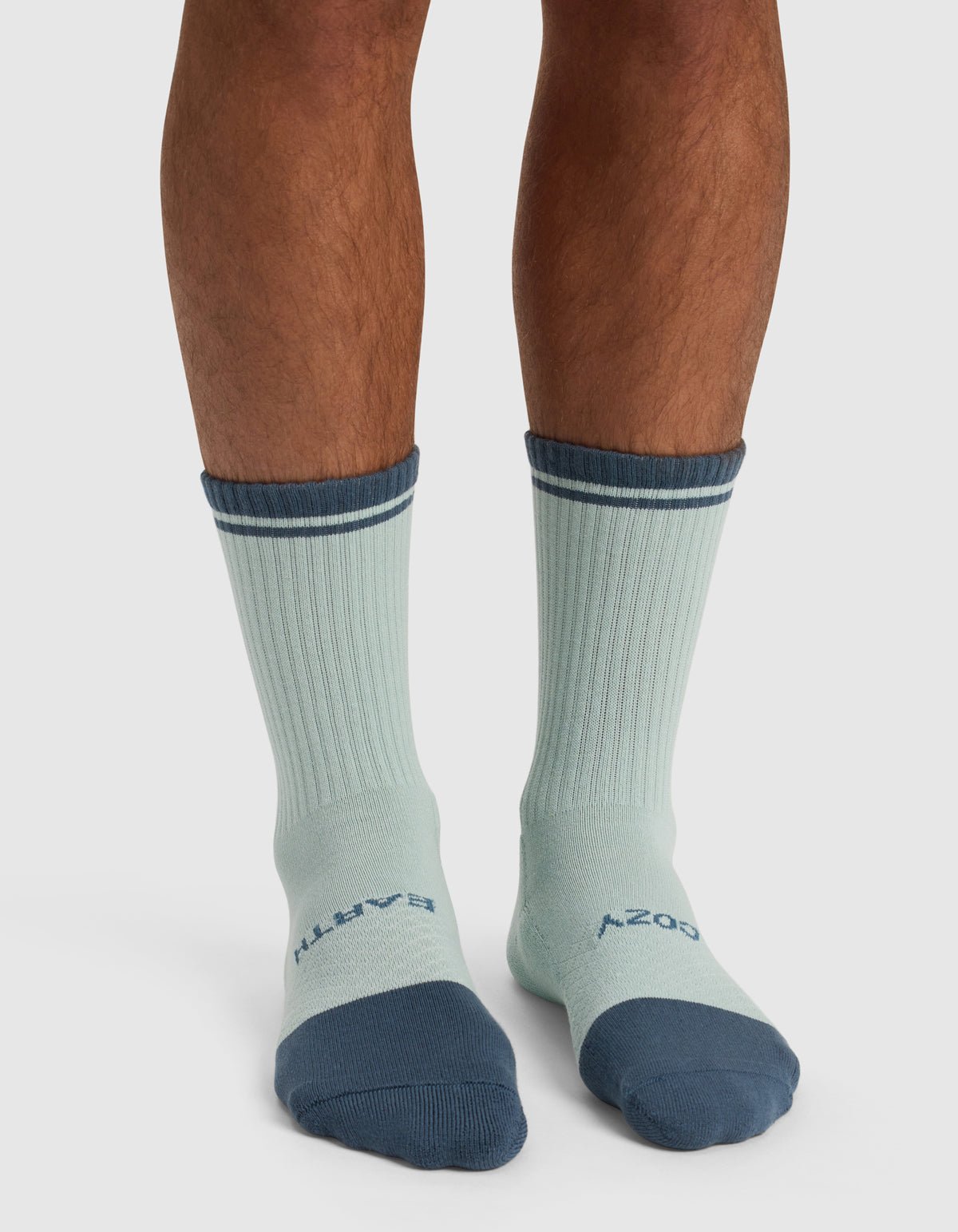 A person wearing Cozy Earth’s Essential Calf Sock – Last Chance in light blue with dark blue toes, heels, and cuffs. "EARTH" is written on the left sock top and "COZY" on the right.|Color:Arctic/Lilac