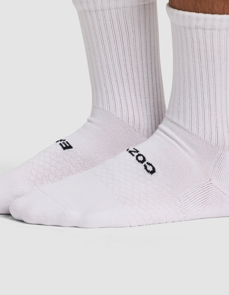 Close-up of a person wearing Cozy Earth Essential Calf Socks. These white ribbed socks feature black text on the top, cover the ankles and lower legs, and are set against a light, plain background.