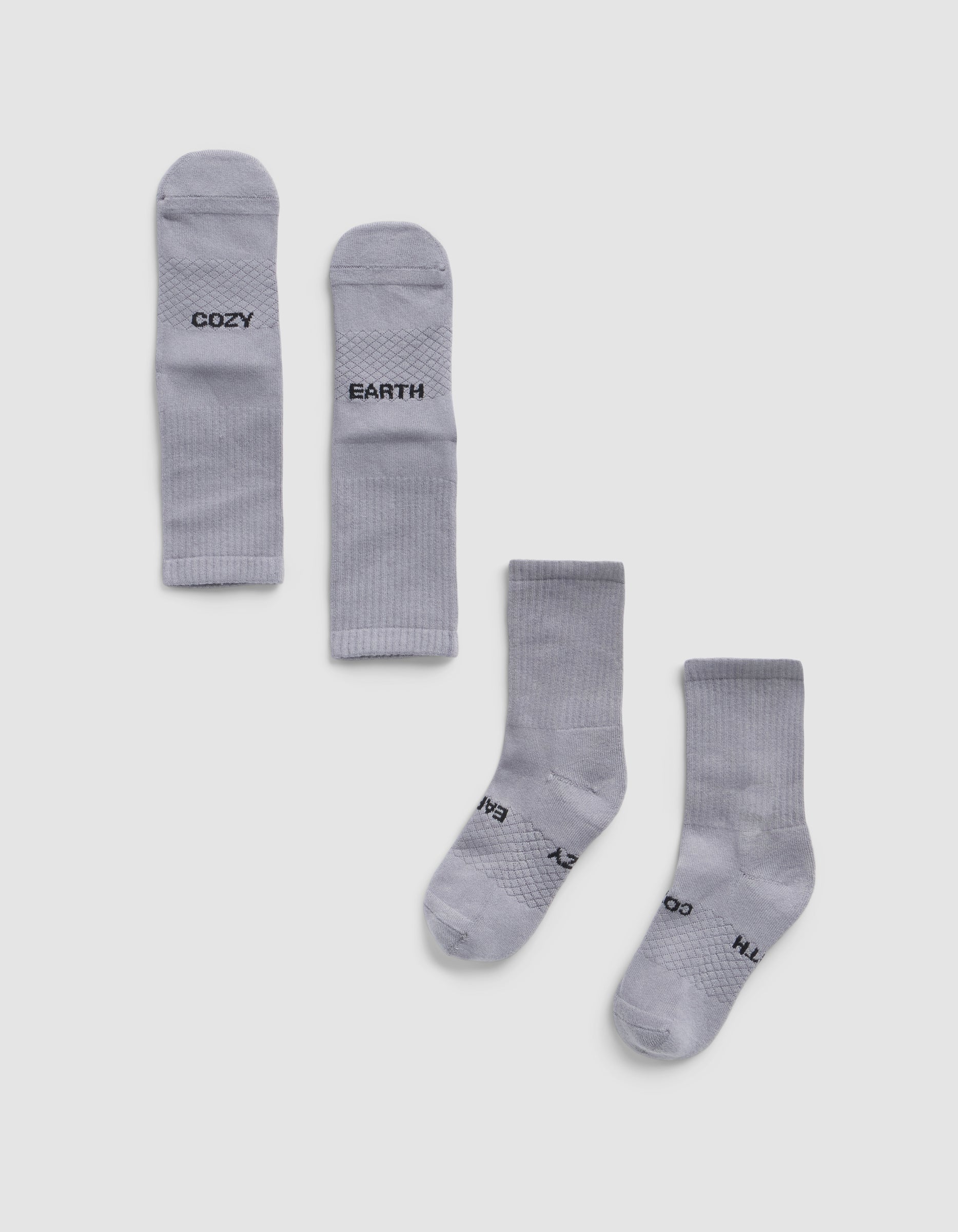 Two pairs of Essential Calf Socks by Cozy Earth are displayed on a white background—one pair folded to show "COZY" and "EARTH," the other flat with the same words visible on the soles.