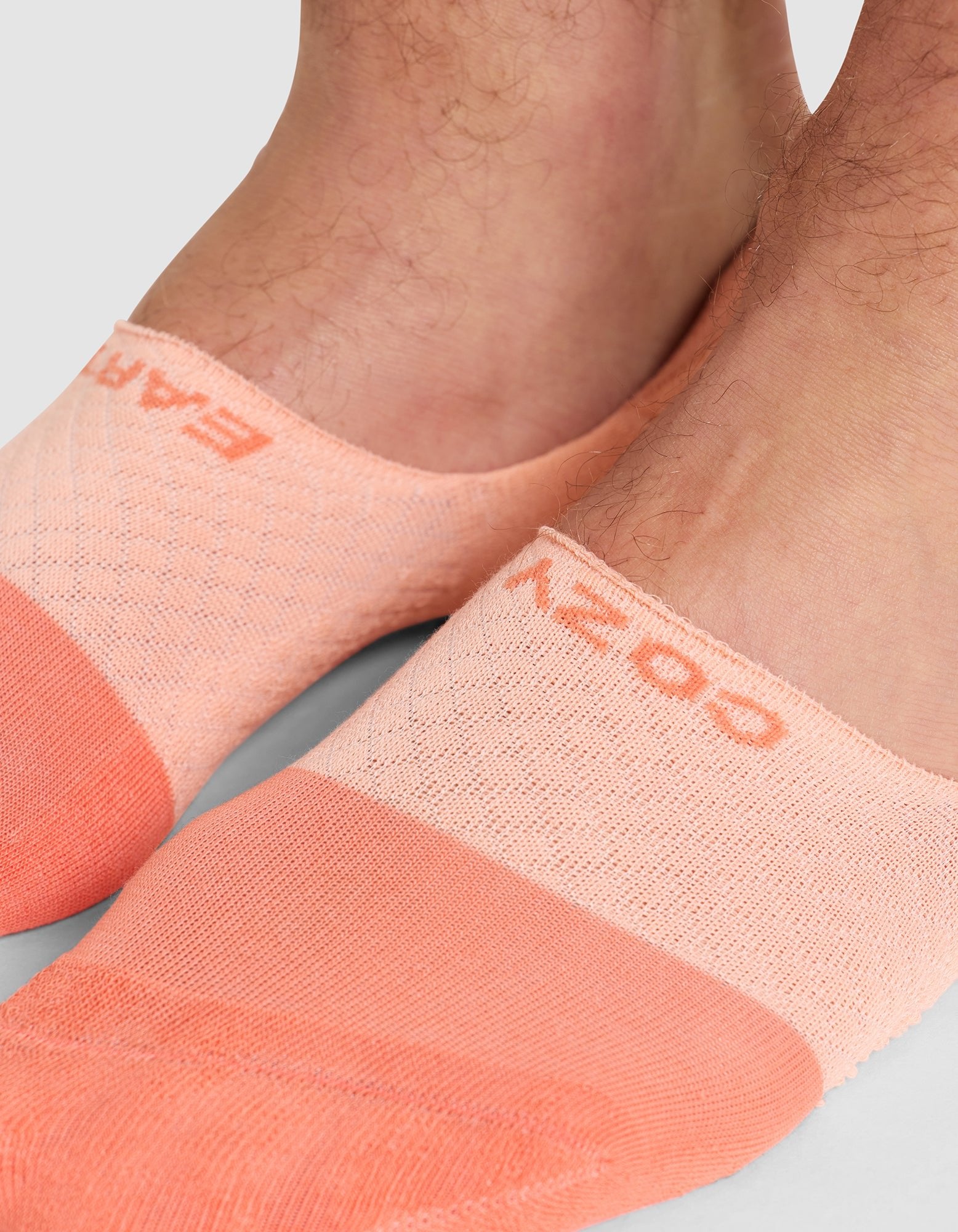 Close-up of two feet wearing Cozy Earth Essential No-Show Socks in peach with textured patterns and "COZY" visible on the top of one sock. |Color:Cantaloupe