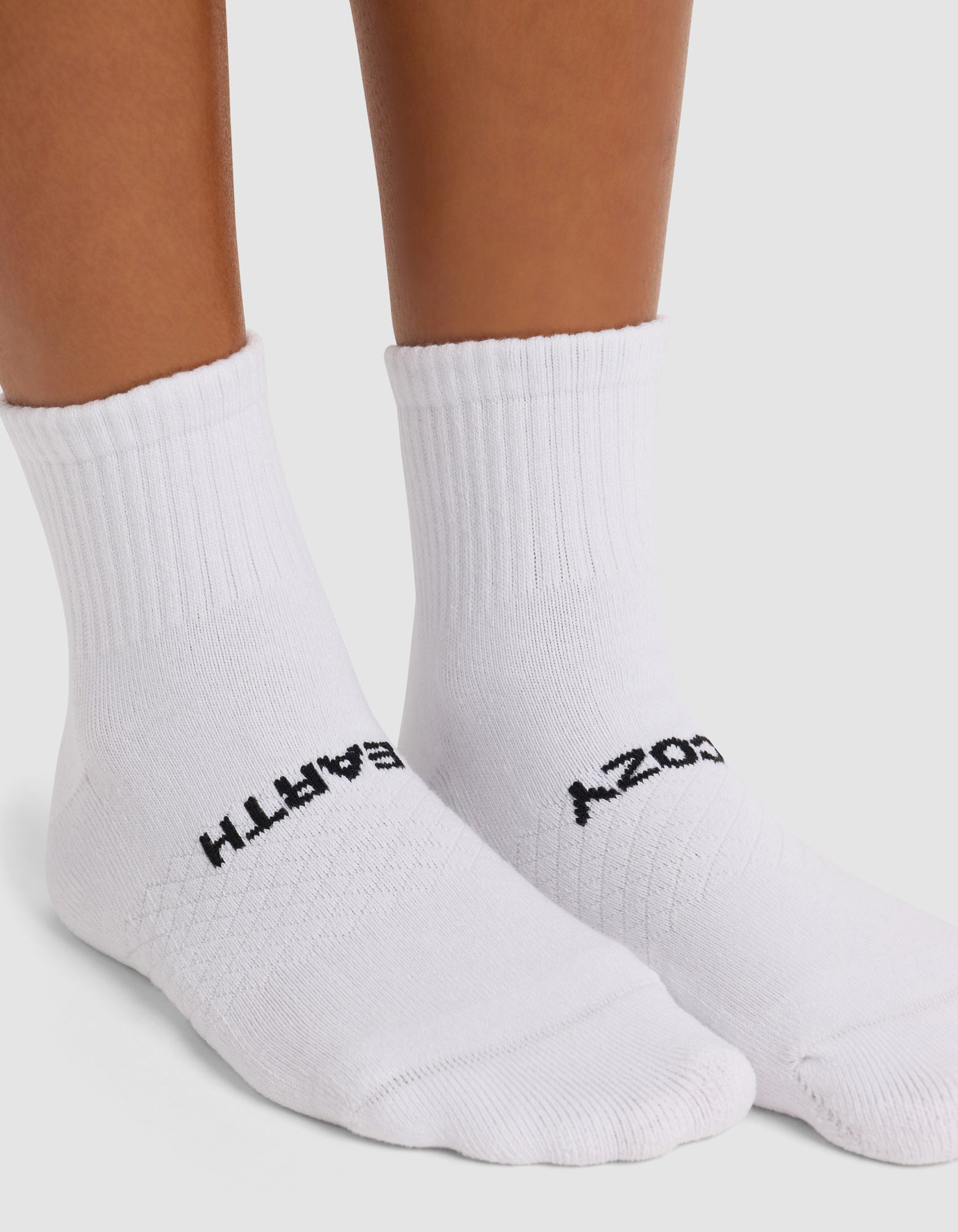 A person stands on a white surface wearing Cozy Earth's Women's Essential Quarter Socks with black "EARTH" text on the left sock and "COZY" on the right, part of the 4-pack set.