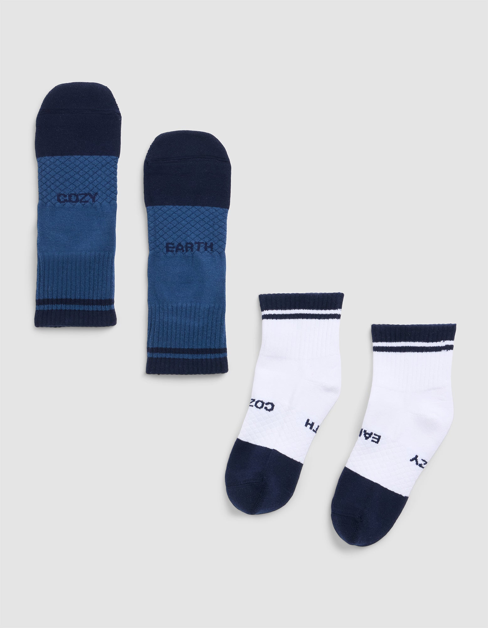 The Cozy Earth Essential Quarter Sock includes two pairs: one blue with navy toes, heels, and cuffs, and one white with navy accents. Both feature the words "COZY" and "EARTH. 