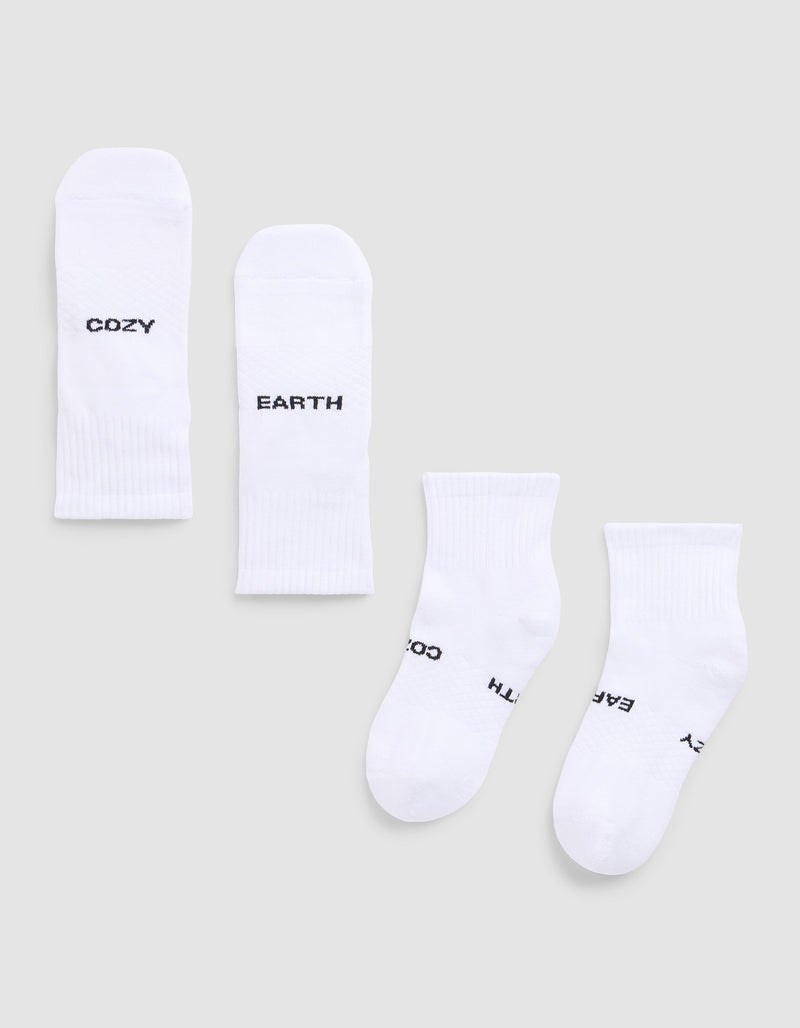 Four white Essential Quarter Socks from Cozy Earth are laid flat on a light gray background. Each features black text: one pair reads “COZY” and “EARTH,” while the other’s text shows parts of “EARTH,” “COZY,”.