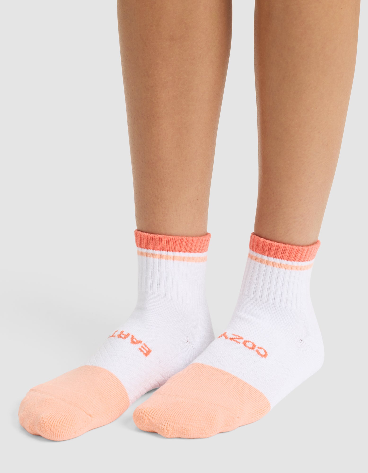 A person wears Cozy Earth Essential Quarter Socks in white with peach toes, heels, and cuffs. The socks feature text on the tops of the feet and are shown against a plain light gray background. |Color:Cantaloupe
