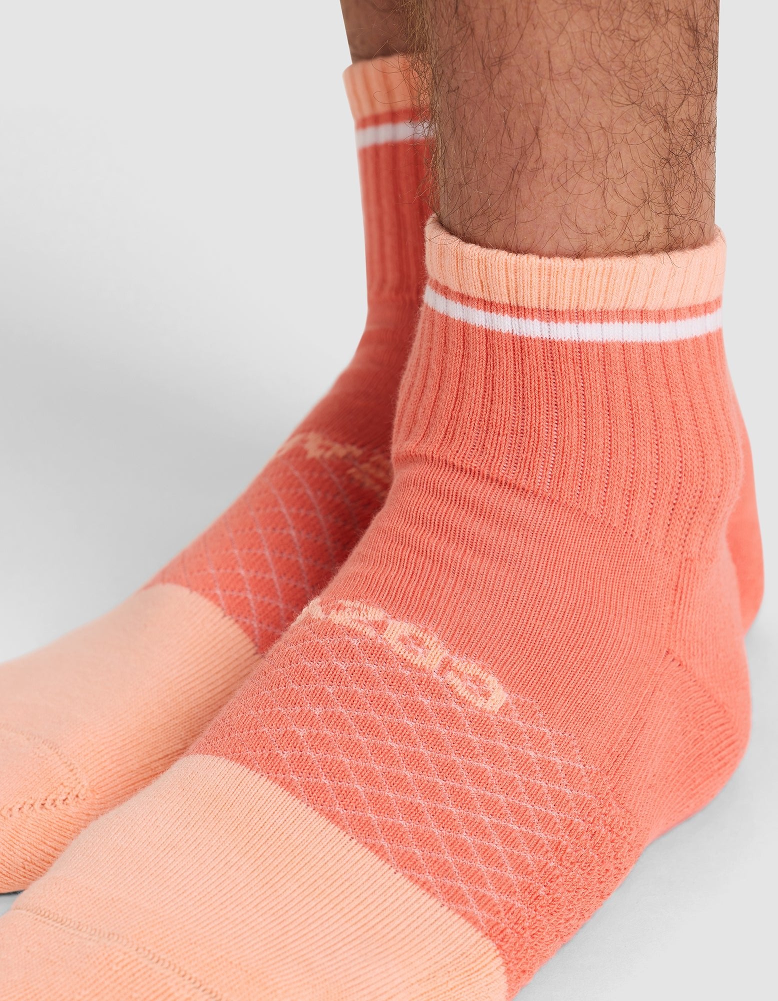 Close-up of a person's lower legs and feet wearing Cozy Earth's Essential Quarter Sock in peach and coral with white stripes. The sock features ribbed ankles and a patterned knit design on the foot. |Color:Cantaloupe